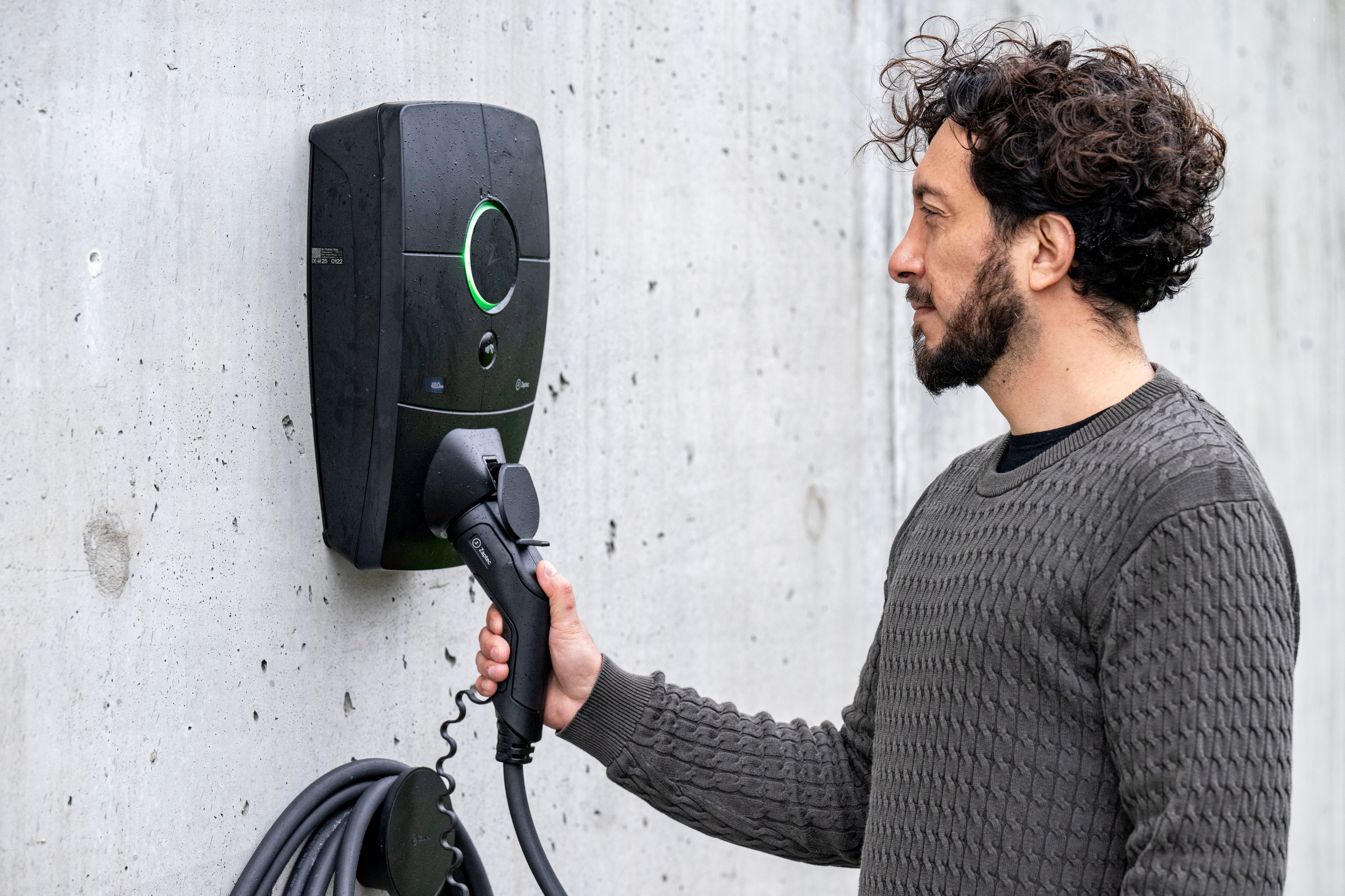 En autoriseret el-installatør fra Vejby A/S ved en Zaptec el-ladestander monteret på en betonvæg.