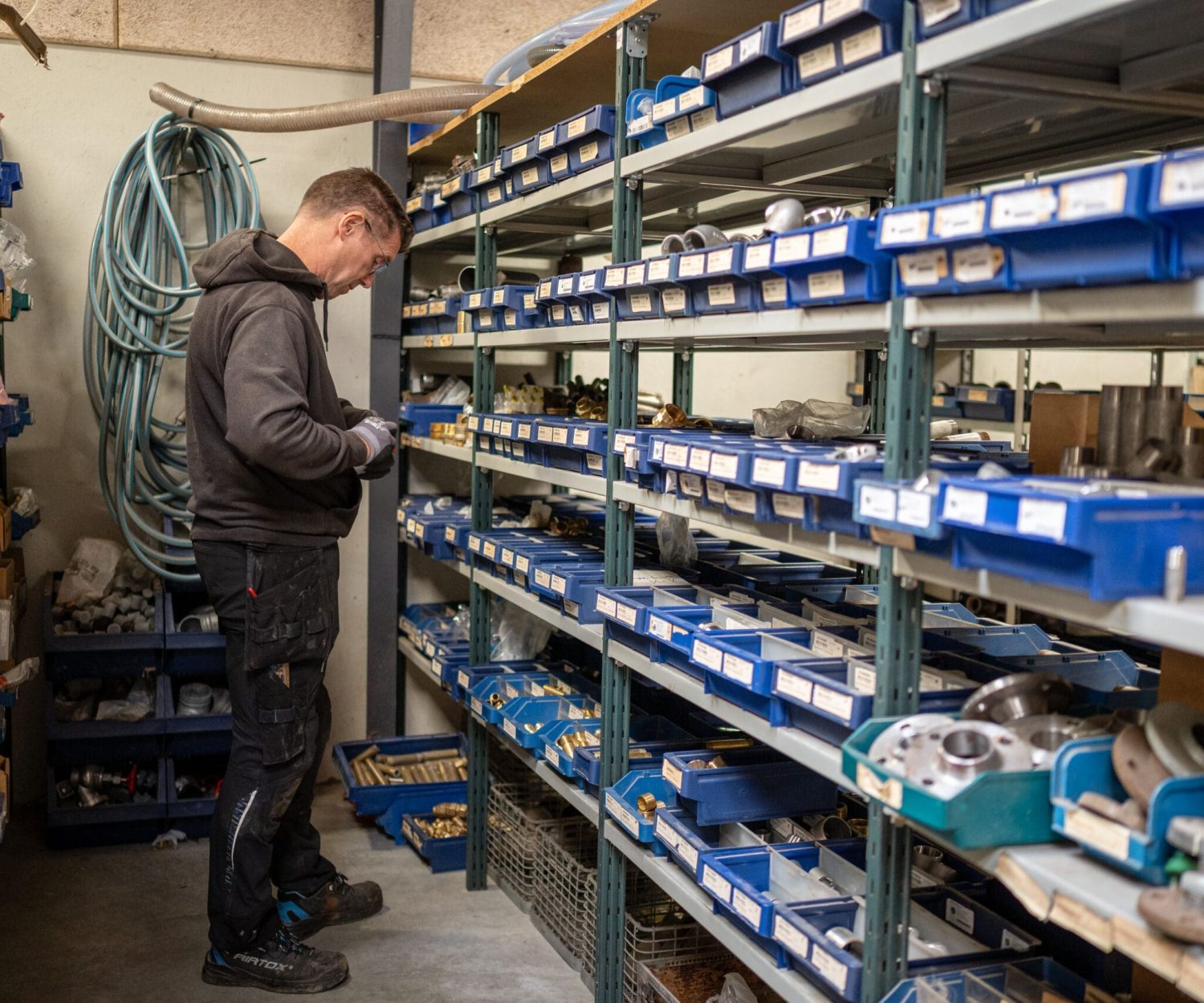 En VVS-medarbejder står ved et lager med VVS-dele i blå kasser på hylder.