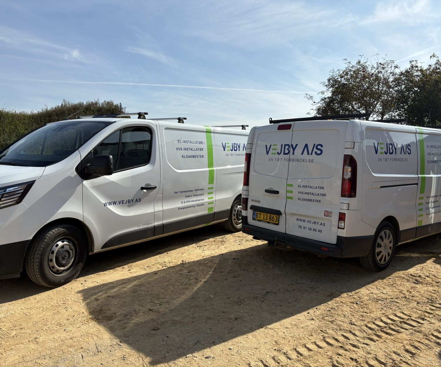 To hvide varevogne med Vejby A/S logo parkeret på en grusplads.